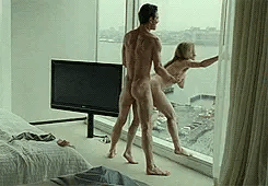 A couple enjoy some sex in their hotel room against the window.